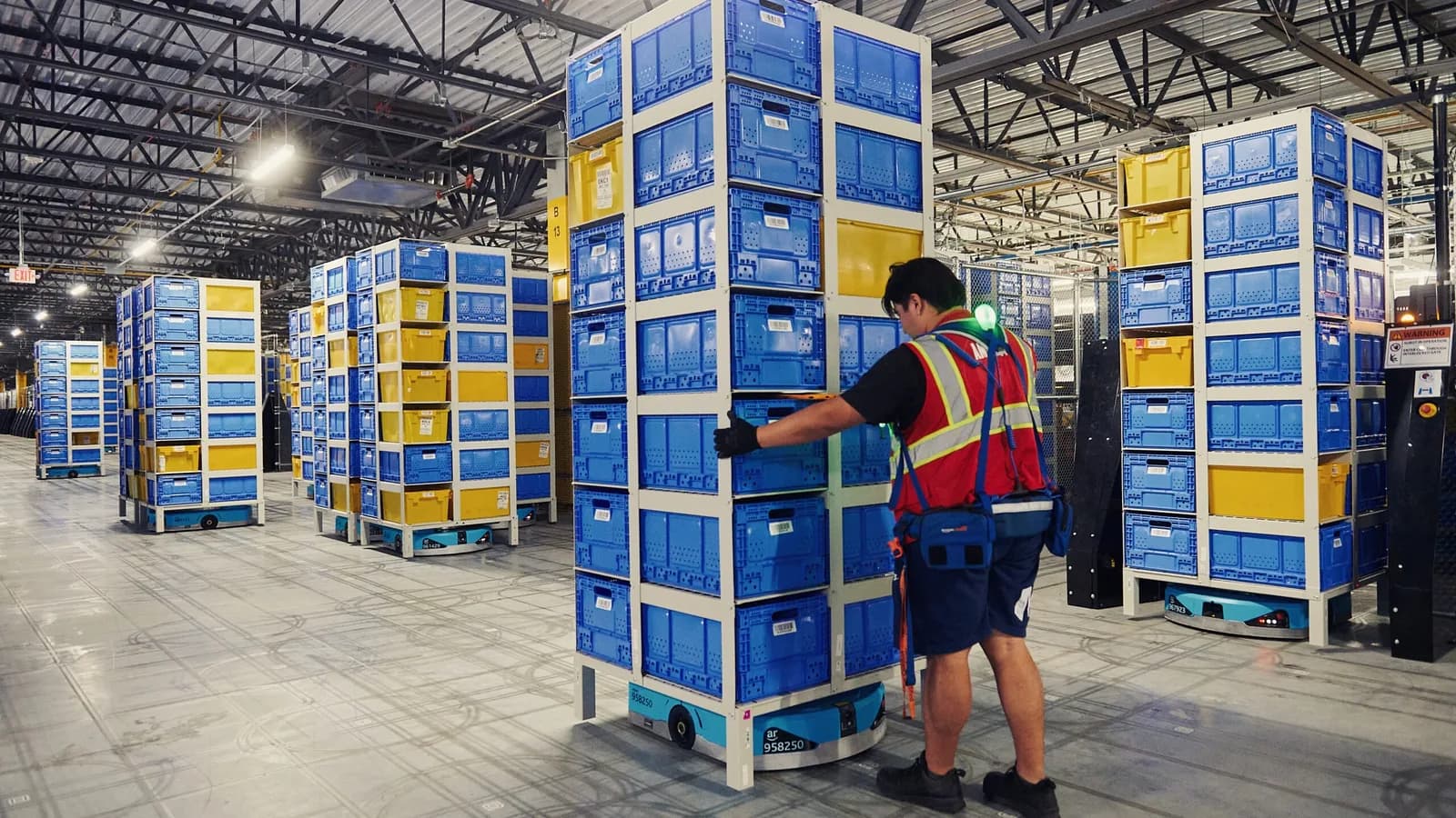 Amazon-ы түгээлтийн төвд барааны өндөр тавиурыг зөөж буй дугуйт робот