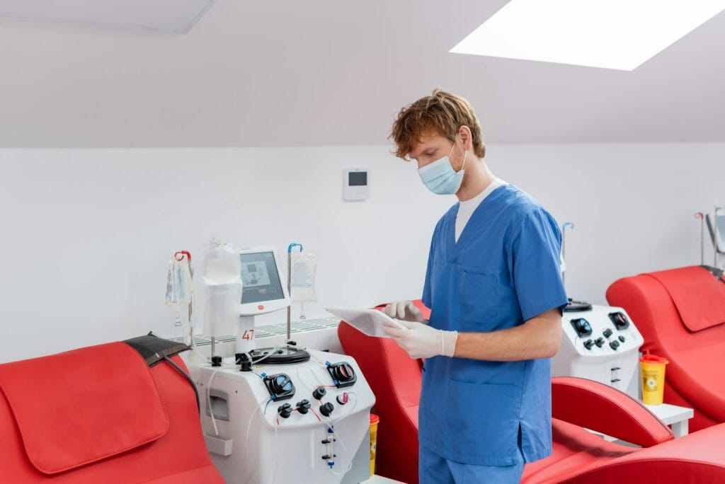 redhead doctor in blue uniform, medical mask and latex gloves looking at digital tablet